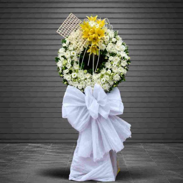 Kệ hoa chia buồn Lưu luyến tông trắng phối hoa ly vàng nổi bật, thiết kế vòng tròn sang trọng thể hiện sự tiếc thương và tiễn biệt.