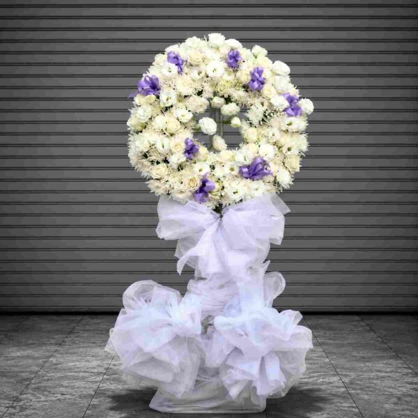 Thương tiếc – vòng hoa chia buồn màu trắng sang trọng kết hợp hoa hồng trắng, cúc trắng và nơ tím, thể hiện lòng thành kính và sự tiếc thương sâu sắc.