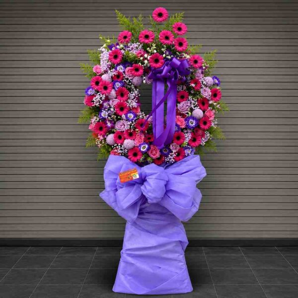 Rest in peace – Kệ hoa chia buồn tông hồng tím nổi bật với hoa đồng tiền hồng, hoa hồng và nơ tím sang trọng