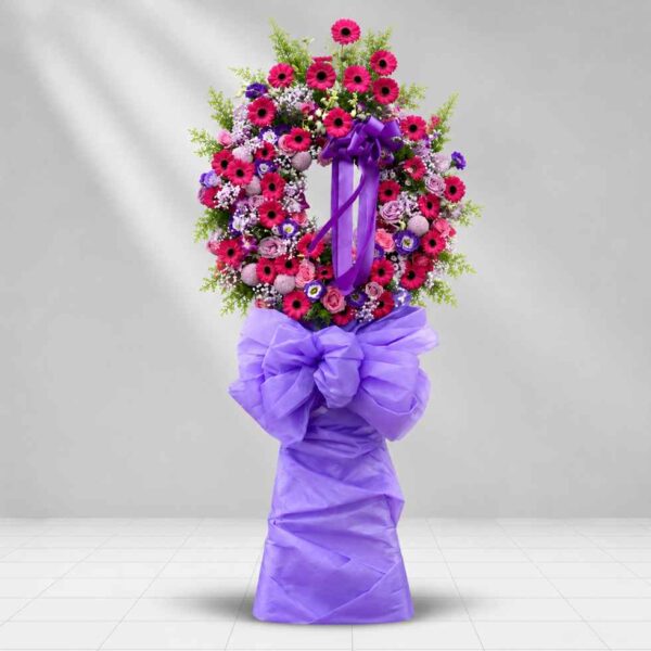Rest in peace – Kệ hoa chia buồn tông hồng tím nổi bật với hoa đồng tiền hồng, hoa hồng và nơ tím sang trọng