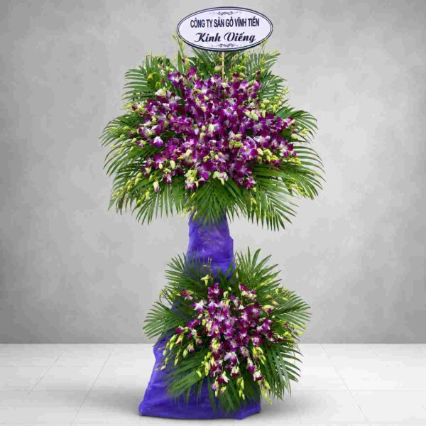 Hoa chia buồn 907 với lan tím nổi bật kết hợp lá cau xanh, thiết kế hai tầng sang trọng thể hiện sự kính trọng và lời chia buồn sâu sắc.