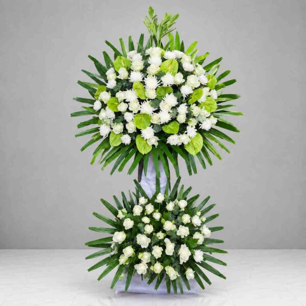 Kệ hoa chia buồn 151 với hoa hồng trắng, cúc trắng và môn xanh, thiết kế hai tầng sang trọng, thể hiện lòng thành kính và sự tiếc thương sâu sắc