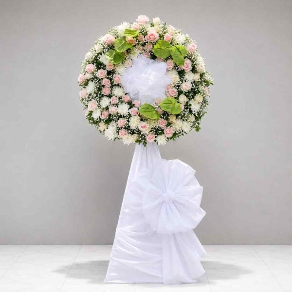 Kệ hoa chia buồn 174 với vòng hoa tông trắng hồng nhẹ nhàng kết hợp hoa hồng pastel, hoa trắng và lá môn xanh sang trọng, mang vẻ đẹp trang nhã.