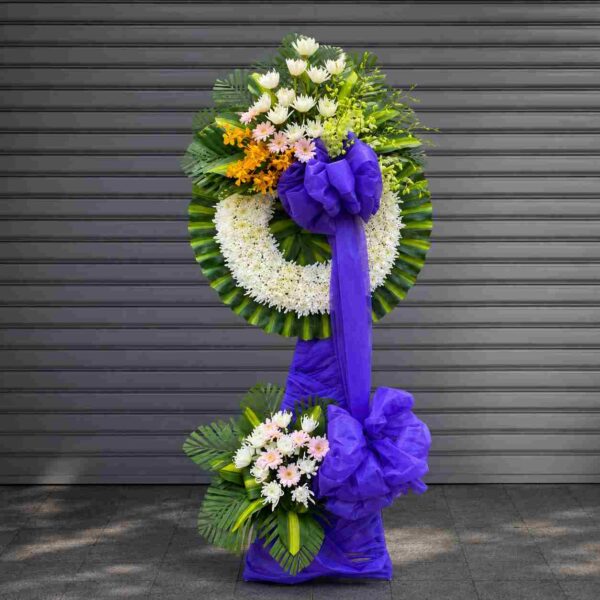 Kệ hoa chia buồn 182 thiết kế vòng hoa tang lễ với hoa trắng, điểm vàng nổi bật và nơ tím sang trọng