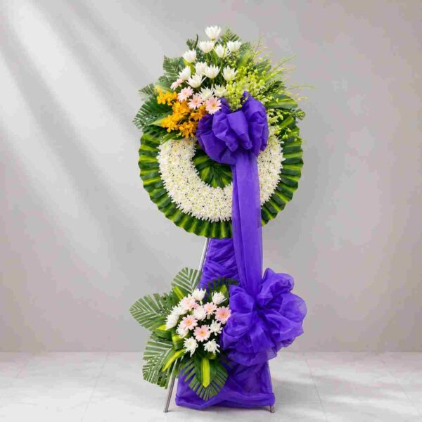 Kệ hoa chia buồn 182 thiết kế vòng hoa tang lễ với hoa trắng, điểm vàng nổi bật và nơ tím sang trọng