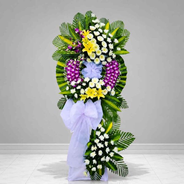 Kệ hoa chia buồn 289 với thiết kế vòng hoa lan tím, hoa ly vàng và cúc trắng nổi bật, kết hợp lá xanh trang trí sang trọng, thể hiện sự tiếc thương và chia sẻ chân thành trong tang lễ.