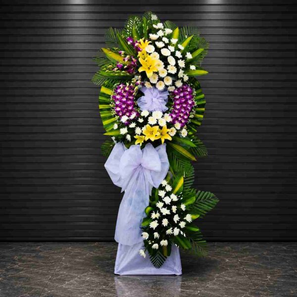 Kệ hoa chia buồn 289 với thiết kế vòng hoa lan tím, hoa ly vàng và cúc trắng nổi bật, kết hợp lá xanh trang trí sang trọng, thể hiện sự tiếc thương và chia sẻ chân thành trong tang lễ.