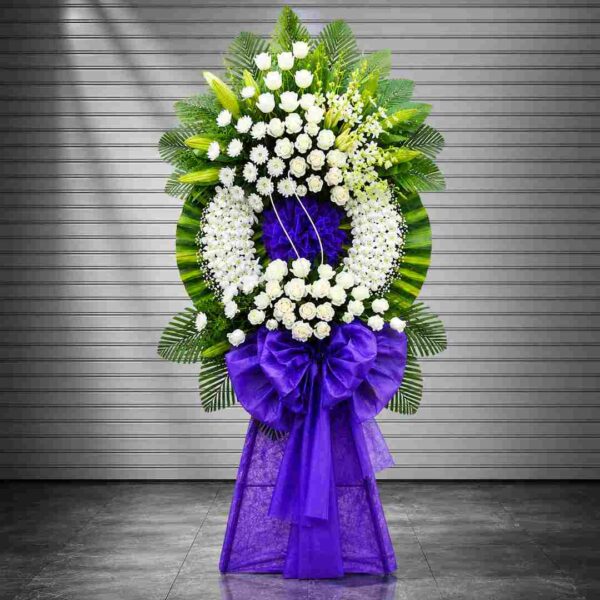 Kệ hoa chia buồn 291 tông trắng phối nơ tím sang trọng với hoa hồng trắng, lan trắng và lá xanh nghệ thuật, mang vẻ trang nghiêm và tinh tế.