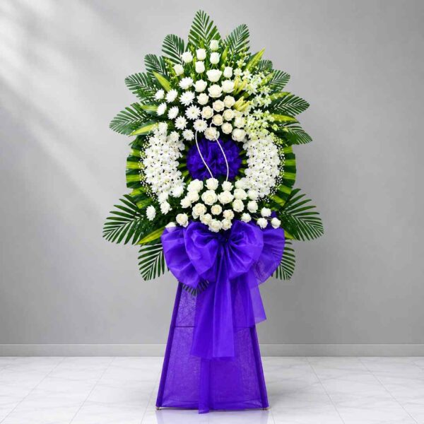 Kệ hoa chia buồn 291 tông trắng phối nơ tím sang trọng với hoa hồng trắng, lan trắng và lá xanh nghệ thuật, mang vẻ trang nghiêm và tinh tế.
