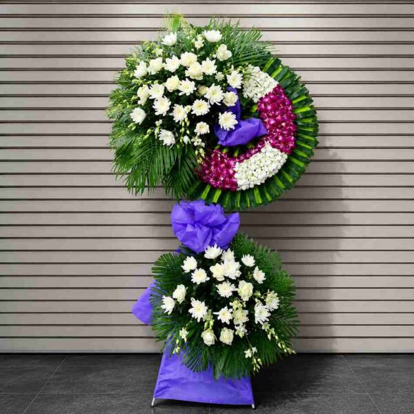 Kệ hoa chia buồn 355 thiết kế hai tầng với hoa trắng kết hợp vòng hoa tím nổi bật, mang phong cách sang trọng và trang nghiêm.