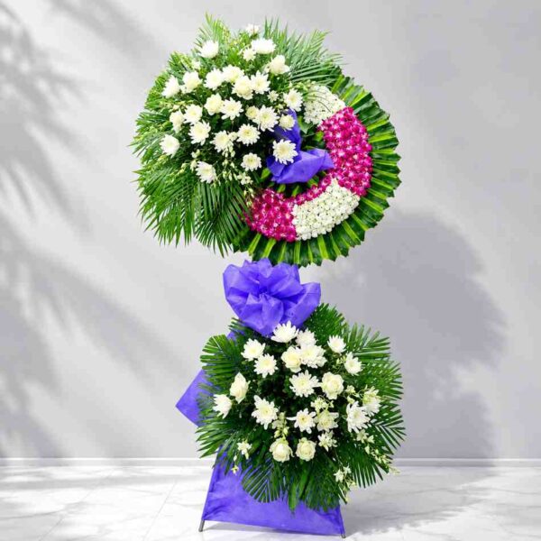 Kệ hoa chia buồn 355 thiết kế hai tầng với hoa trắng kết hợp vòng hoa tím nổi bật, mang phong cách sang trọng và trang nghiêm.