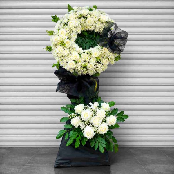 Kệ hoa chia buồn 345 tone trắng sang trọng với vòng hoa cúc, hoa hồng trắng kết hợp lá xanh và nơ đen trang nhã.