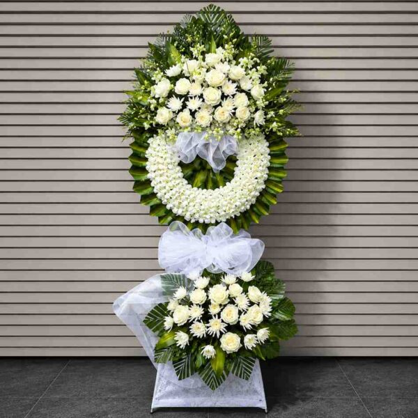 Kệ hoa chia buồn 383 thiết kế hai tầng với hoa hồng trắng, hoa cúc trắng và vòng hoa viếng sang trọng, mang phong cách trang nghiêm và tinh tế.