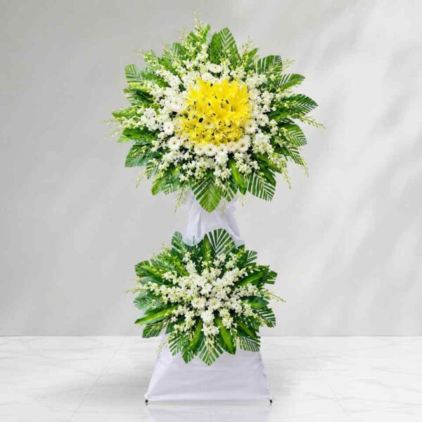 Kệ hoa chia buồn 412 với hoa ly vàng nổi bật kết hợp hoa trắng và lá xanh tươi, thiết kế hai tầng sang trọng thể hiện sự tiếc thương và chia sẻ sâu sắc.