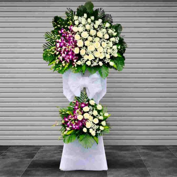 Kệ hoa chia buồn 497 tông trắng tím sang trọng với hoa hồng trắng, lan tím và lá xanh trang trí trang nghiêm