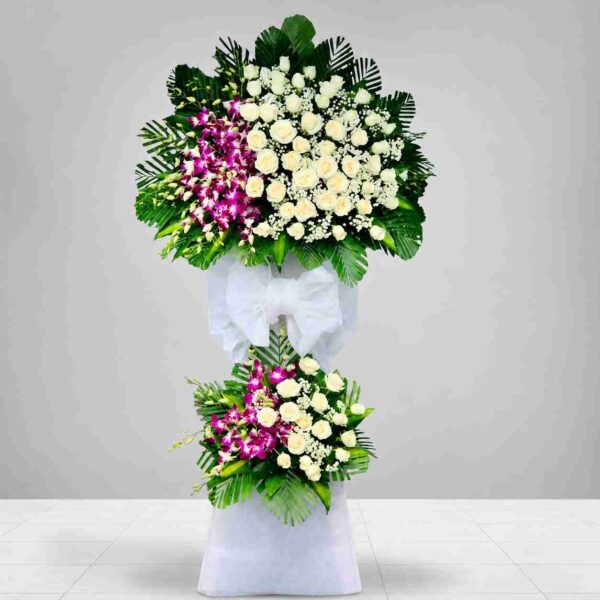 Kệ hoa chia buồn 497 tông trắng tím sang trọng với hoa hồng trắng, lan tím và lá xanh trang trí trang nghiêm