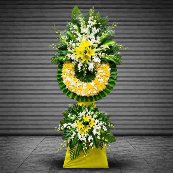 Kệ hoa chia buồn 514 với hoa ly vàng, lan trắng và vòng hoa vàng trắng trang trọng, thiết kế hai tầng sang trọng thể hiện sự tiếc thương và kính viếng sâu sắc.