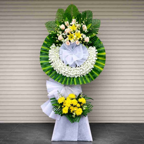 Kệ hoa chia buồn 451 thiết kế vòng hoa tang lễ màu trắng phối vàng, nổi bật với hoa lan trắng, hoa ly vàng, hoa hồng kem và lá xanh sang trọng, thể hiện sự kính trọng và tiếc thương sâu sắc.