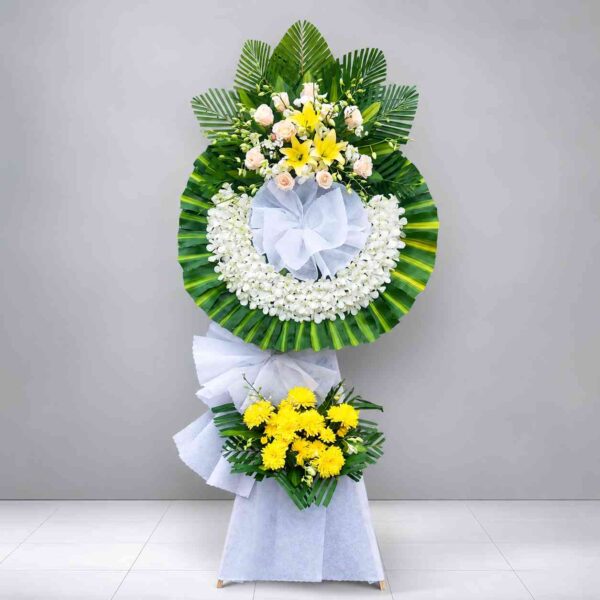 Kệ hoa chia buồn 451 thiết kế vòng hoa tang lễ màu trắng phối vàng, nổi bật với hoa lan trắng, hoa ly vàng, hoa hồng kem và lá xanh sang trọng, thể hiện sự kính trọng và tiếc thương sâu sắc.