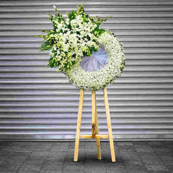 Kệ hoa chia buồn 491 tông trắng trang nhã, thiết kế vòng hoa tròn kết từ hoa lan trắng kết hợp lá xanh và chân gỗ tự nhiên, thể hiện sự thành kính và chia buồn sâu sắc.
